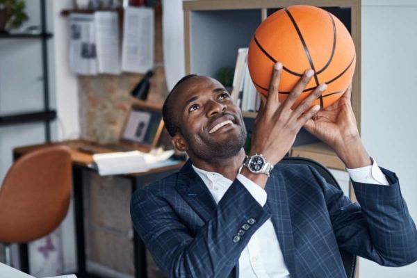 Man at desk in office sitting in chair with basketball in shooting pose